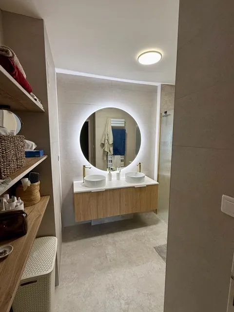 Meuble vasque en bois et miroir rond lumineux dans une salle de bain rénovée