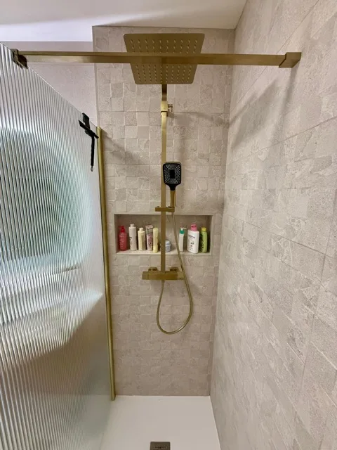 Douche avec robinetterie dorée, paroi texturée et niche murale